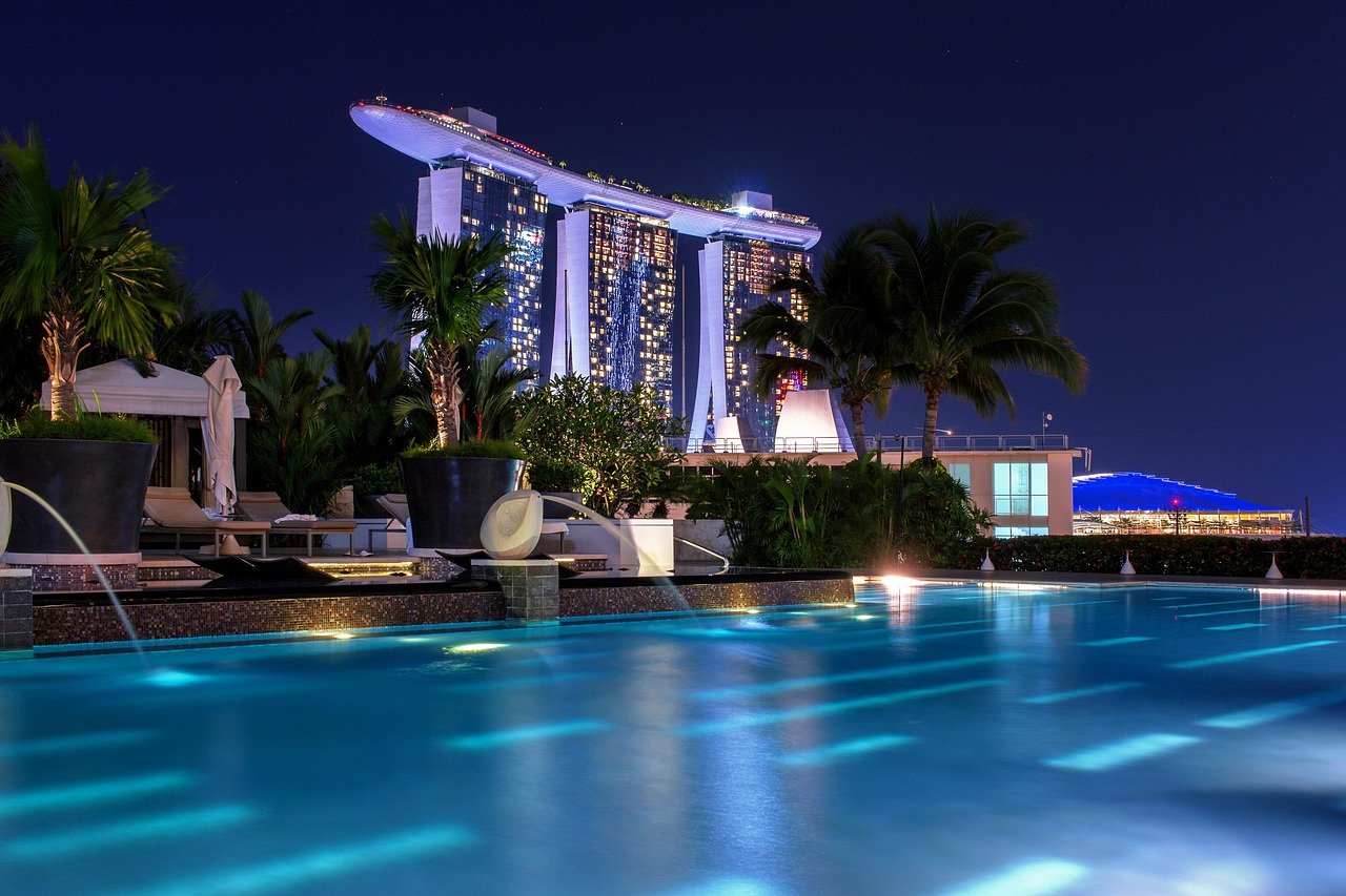 Night view of Marina Bay Sands hotel and illuminated rooftop pool in Singapore with palm trees and blue water