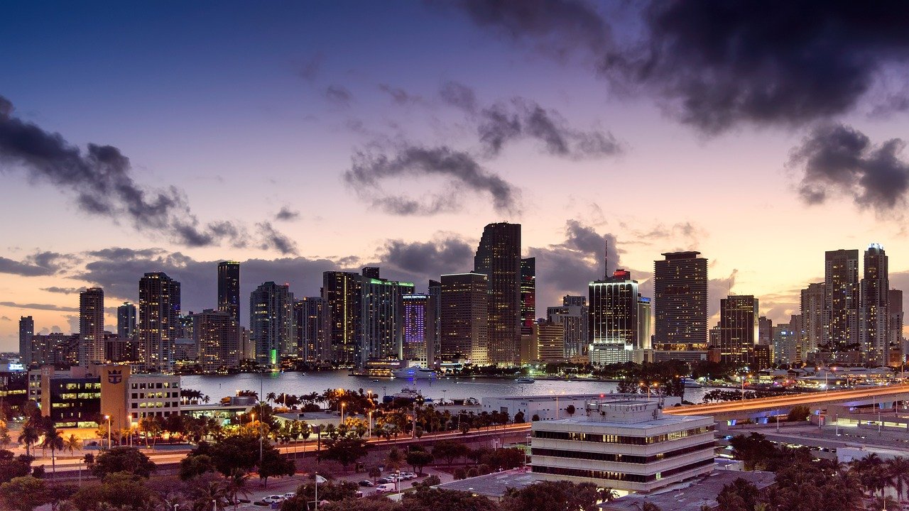 Miami city skyline at dusk with illuminated skyscrapers and waterfront view under a cloudy purple sky