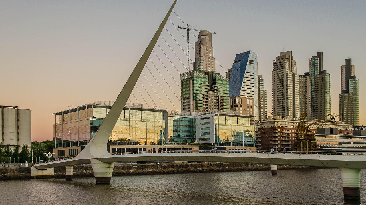 Modern cable-stayed bridge over river with city skyline and high-rise buildings at sunset in urban area