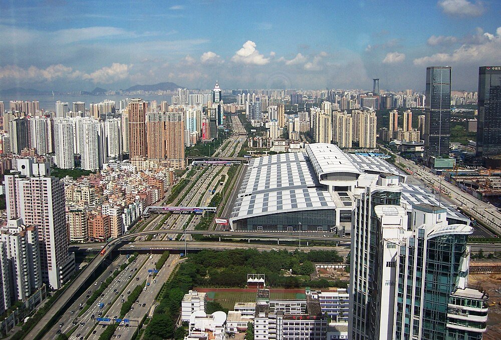 Aerial view of a modern cityscape with high-rise buildings, busy highways, and a large convention center under a blue sky.