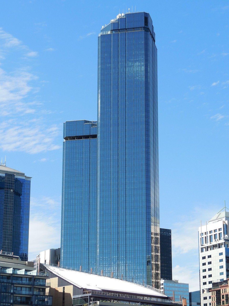 Tall modern glass skyscraper reflecting blue sky in urban cityscape with surrounding buildings under clear weather