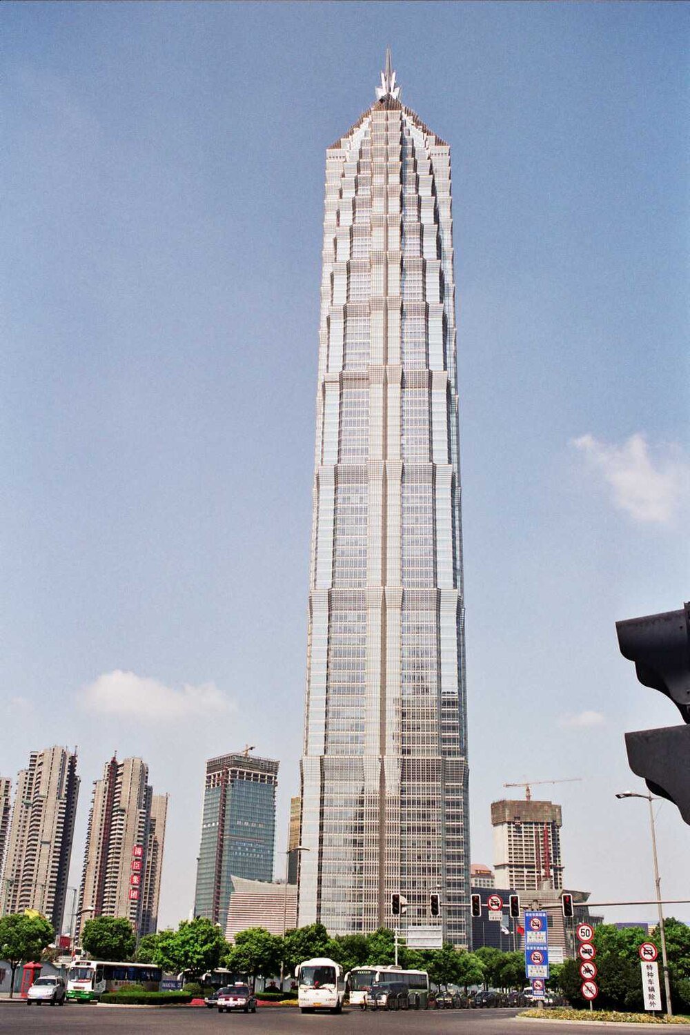 Modern skyscraper in urban cityscape Tall modern skyscraper in a city with clear blue sky and surrounding buildings, traffic lights, and vehicles on the road