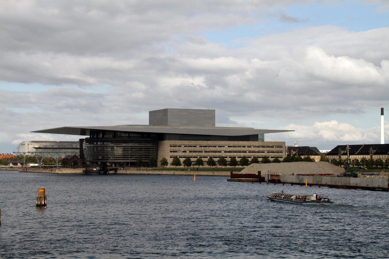 Modern waterfront building with unique architectural design and a boat sailing on the water under cloudy sky