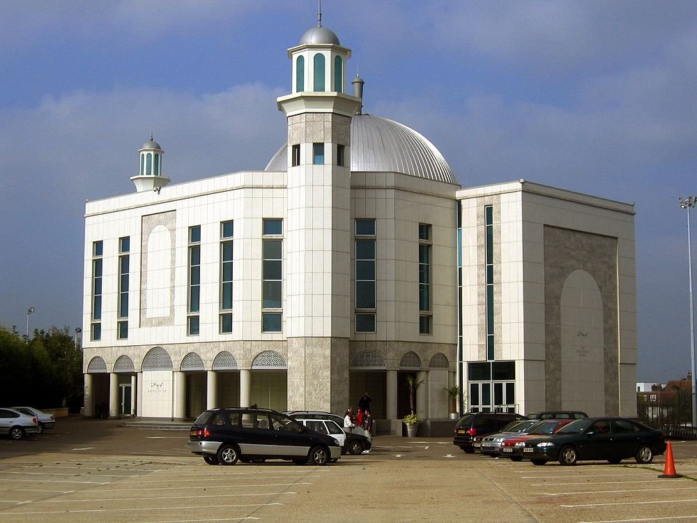 Modern white mosque with dome and minarets Modern white mosque with dome and minarets in a parking lot under a cloudy sky with several parked cars