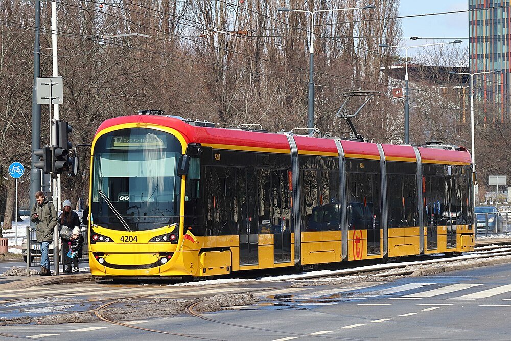 Modern yellow and red tram 4204 on city street with passengers waiting at tram stop in winter