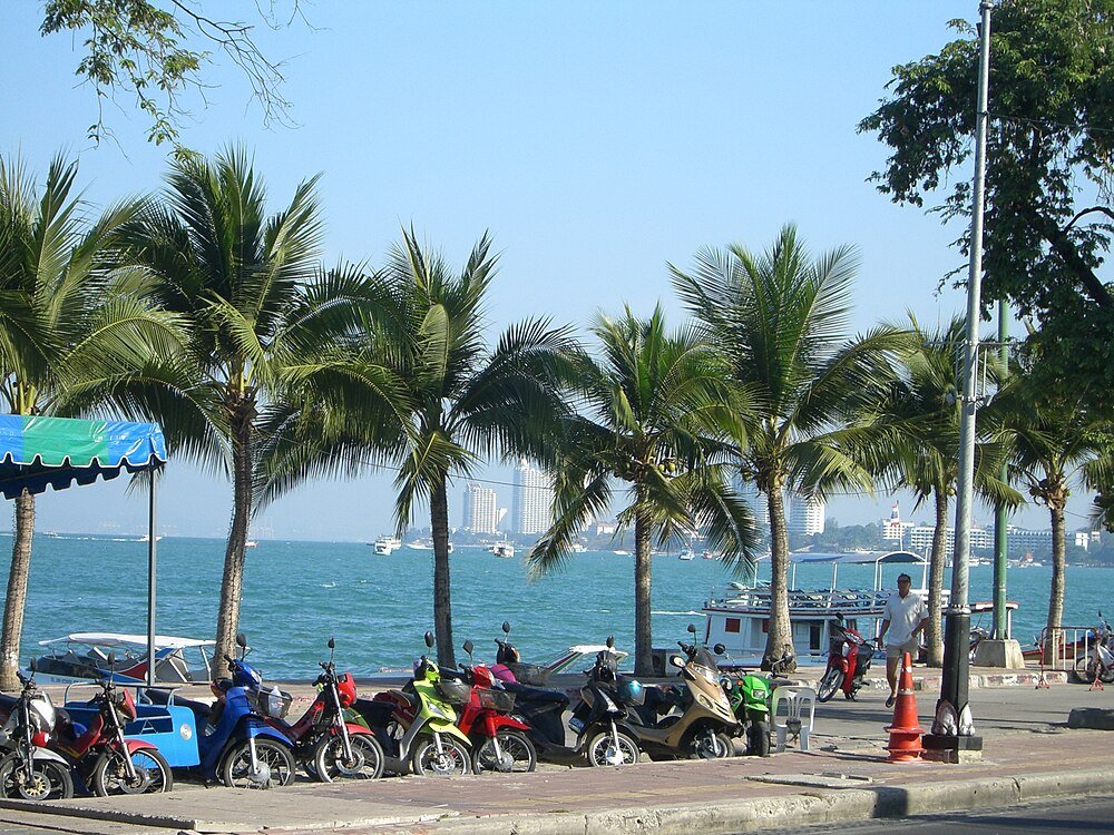 Colorful motorbikes parked by the seaside with palm trees Row of colorful motorbikes parked along a seaside promenade with palm trees and blue ocean under clear sky