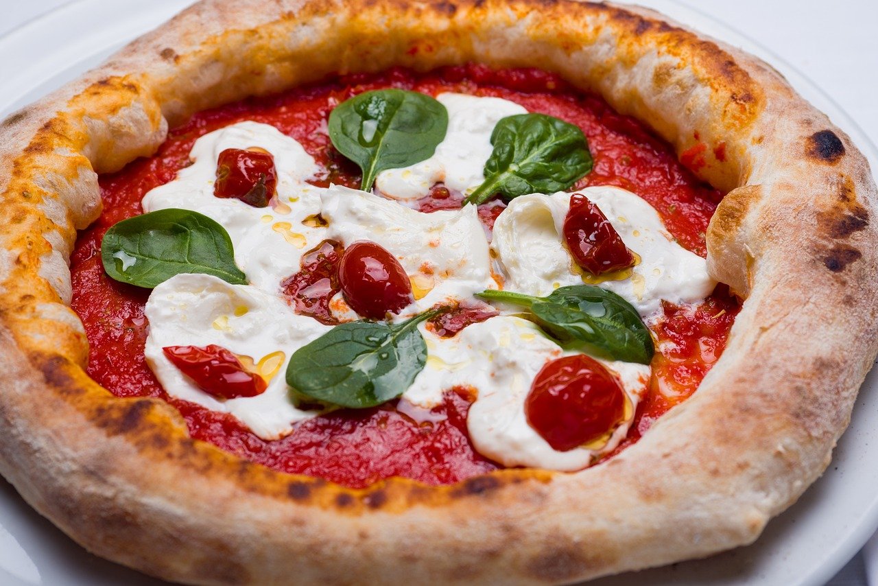 Close-up of a delicious Neapolitan pizza with fresh tomato sauce, mozzarella cheese, spinach leaves, and cherry tomatoes