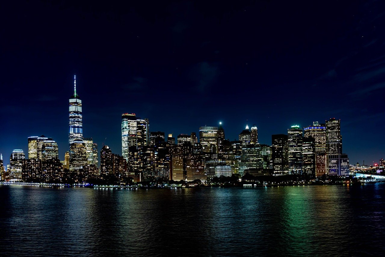 Nighttime view of New York City skyline with illuminated skyscrapers and reflections on the water