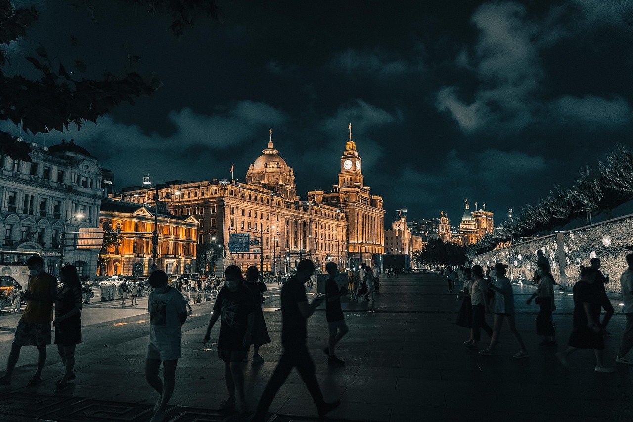 Nighttime cityscape with illuminated historic buildings and people walking on a busy street