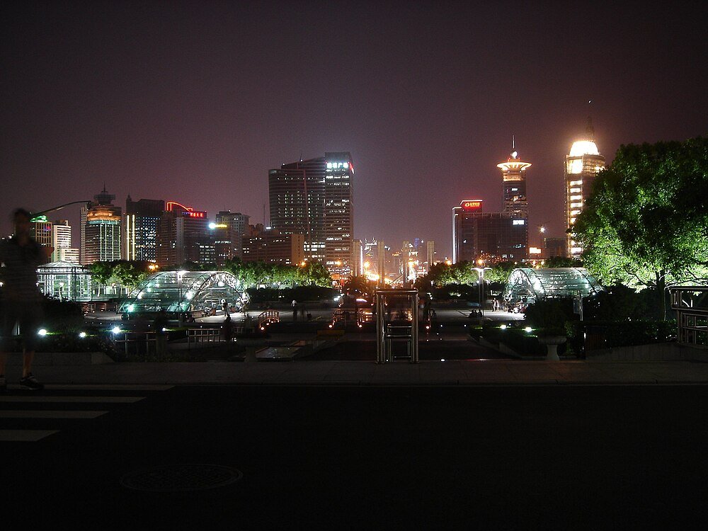 Night city skyline with illuminated buildings and park Night cityscape with illuminated skyscrapers, modern glass structures, and trees in an urban park setting