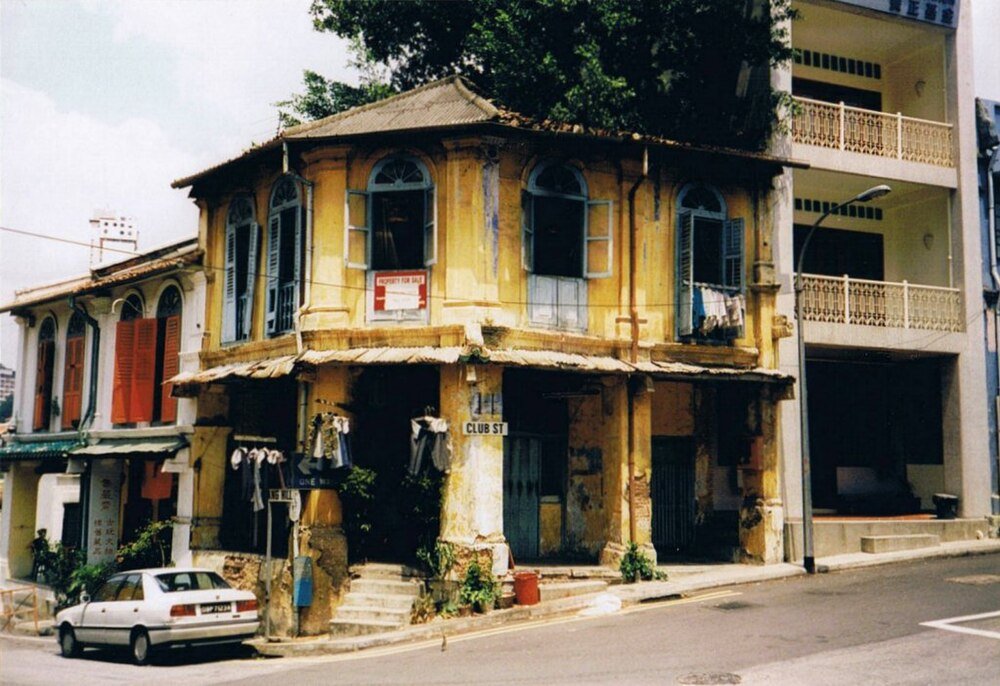 Old colonial building on Club Street with vintage car Old yellow colonial building with arched windows and shutters on Club Street, vintage car parked nearby in urban setting