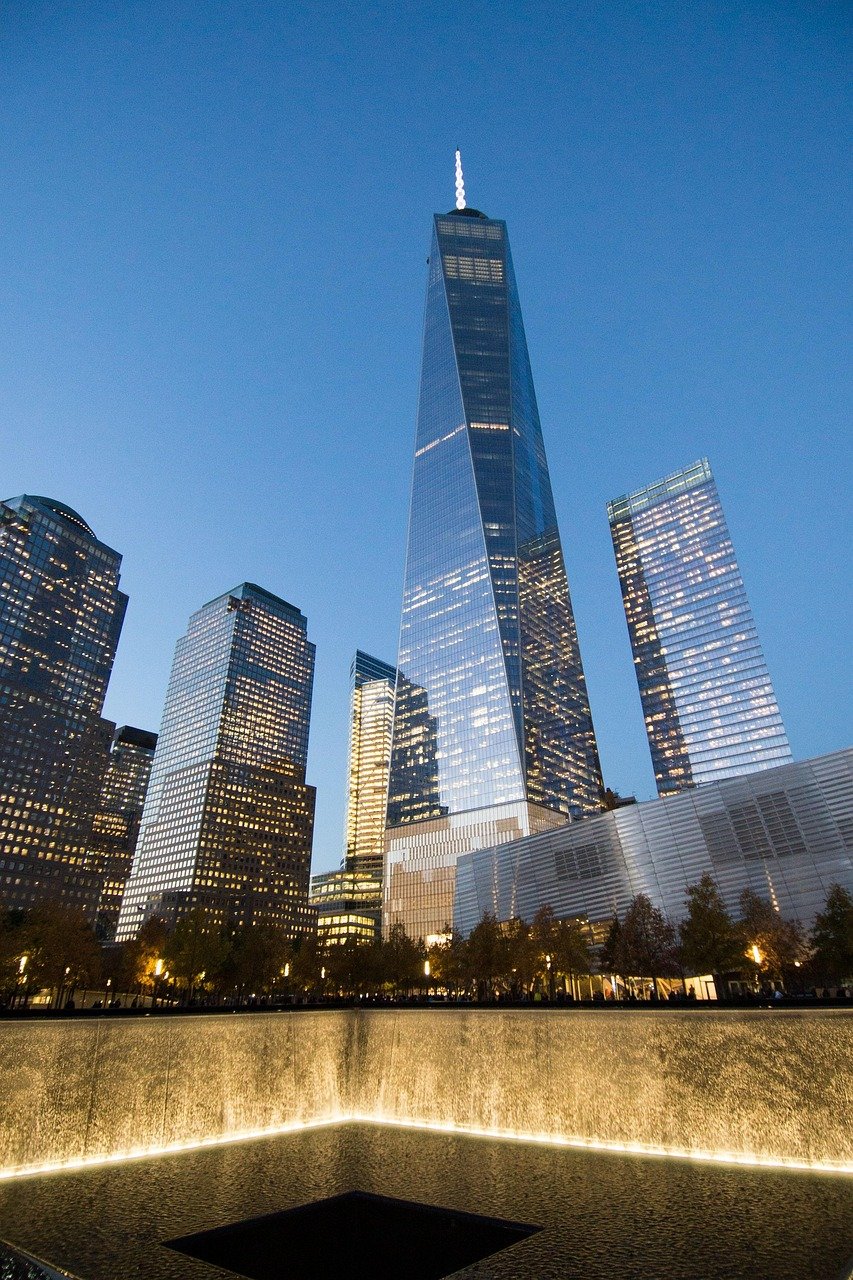 One World Trade Center and 9/11 Memorial reflecting in water at dusk in New York City skyline