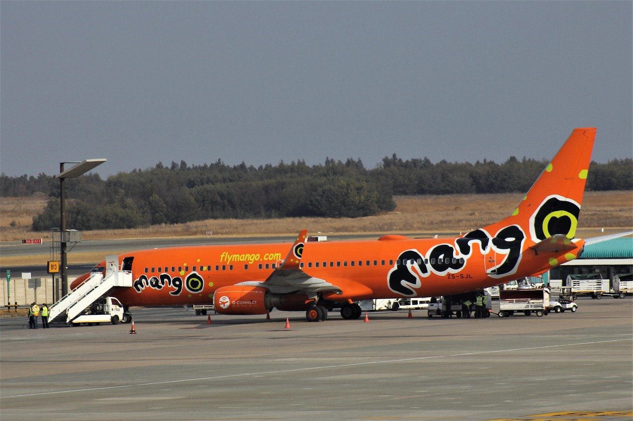 Orange Mango Airlines airplane parked at airport gate with boarding stairs and ground crew preparing for departure