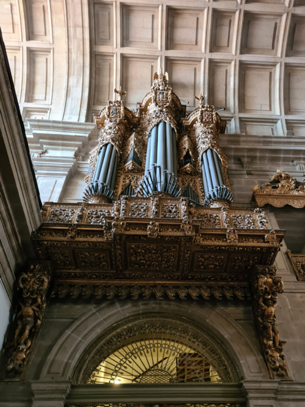 Ornate antique pipe organ with intricate gold carvings inside a historic cathedral with stone arches