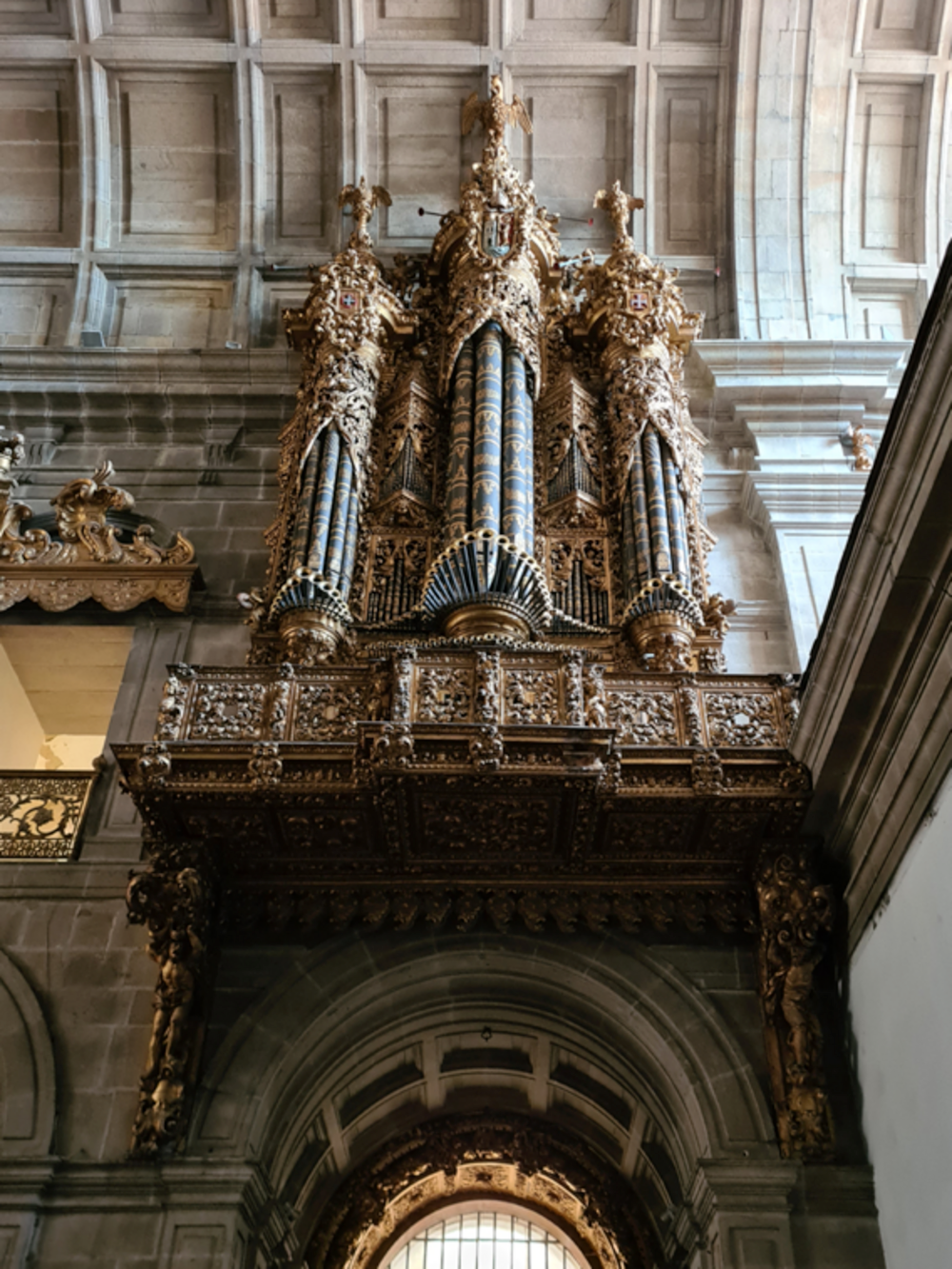 Ornate golden pipe organ with blue and gold decorated pipes inside historic stone cathedral