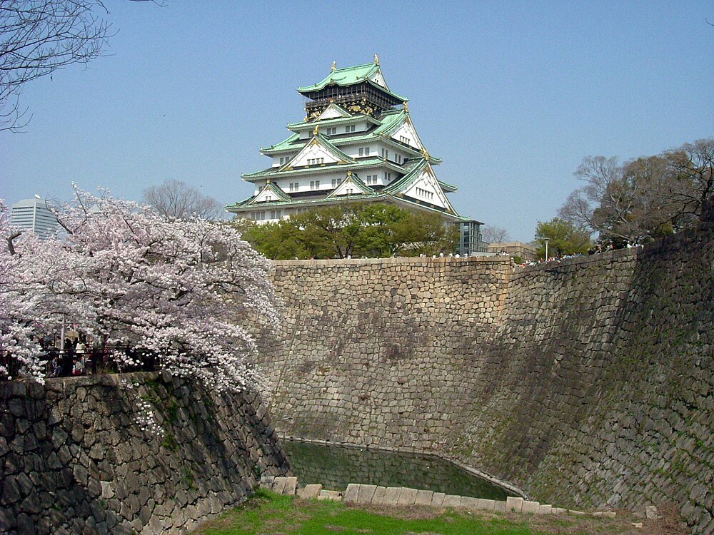 Osaka Castle with Cherry Blossoms Osaka Castle surrounded by cherry blossom trees and stone walls under a clear blue sky in Japan