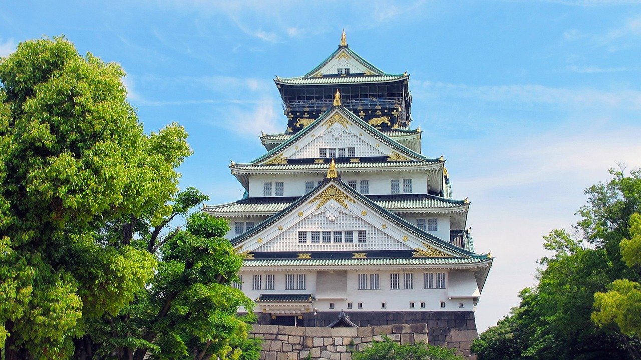 Osaka Castle in Japan surrounded by green trees under a clear blue sky, showcasing traditional Japanese architecture