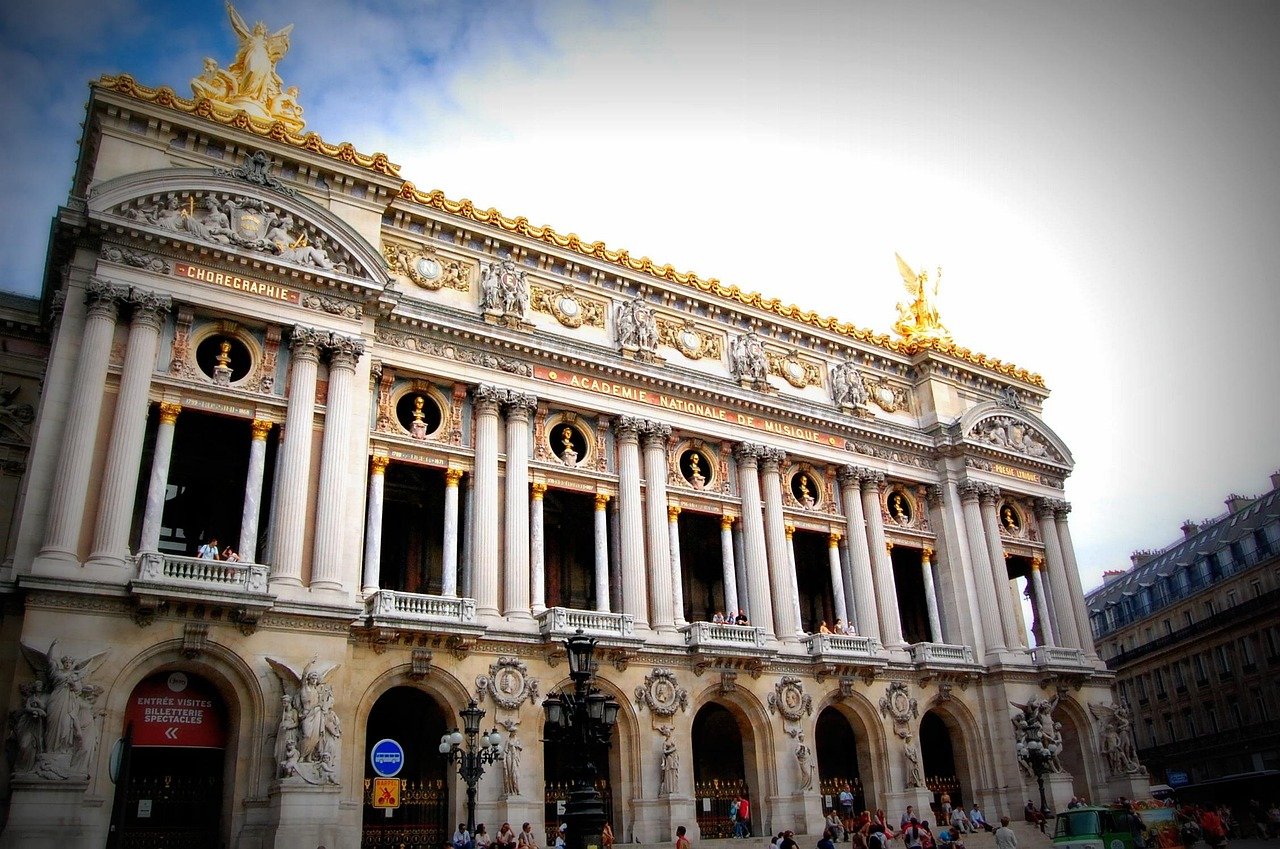 Facade of the Palais Garnier opera house in Paris with ornate columns and golden statues under a blue sky