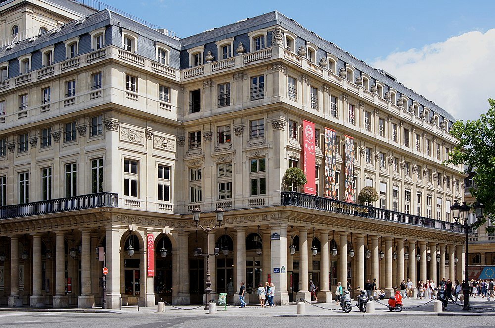 Palais Royal historic building in Paris Historic Palais Royal building with classical columns and detailed architecture in Paris, France, bustling with pedestrians and scooters.