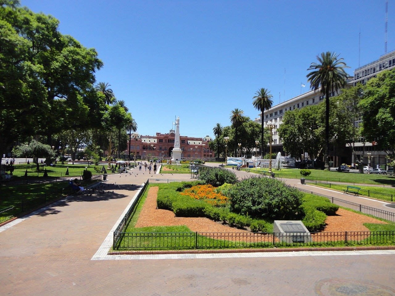 Sunny day view of Plaza de Mayo with green gardens, palm trees, and Casa Rosada presidential palace in Buenos Aires