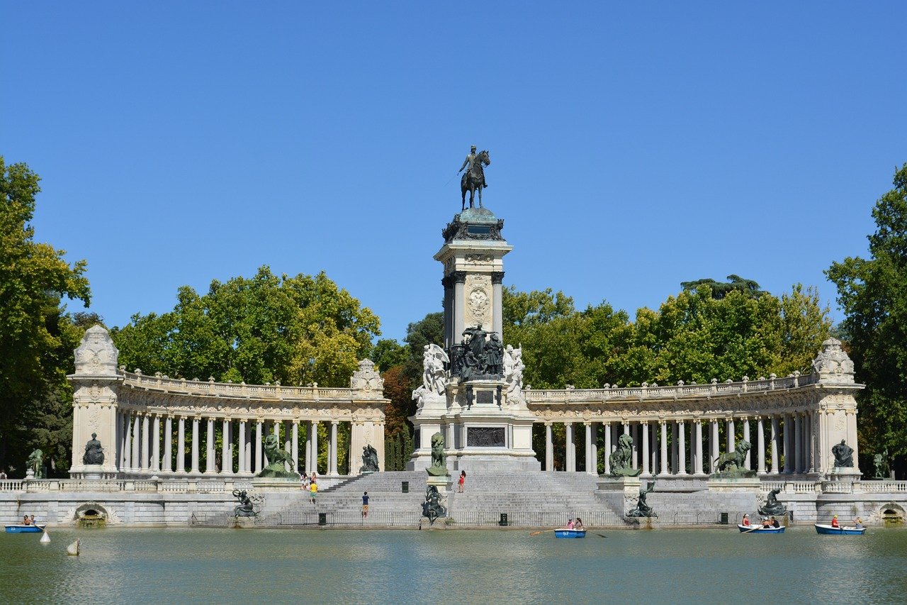 Monument with equestrian statue and colonnade at Retiro Park in Madrid with people boating on the lake