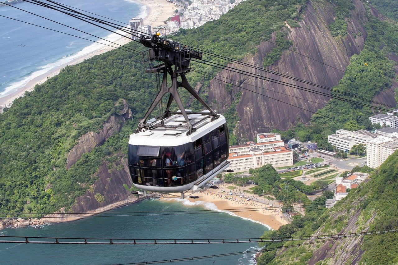 Cable car transporting tourists over lush green mountains and beaches in Rio de Janeiro, Brazil with ocean and city views