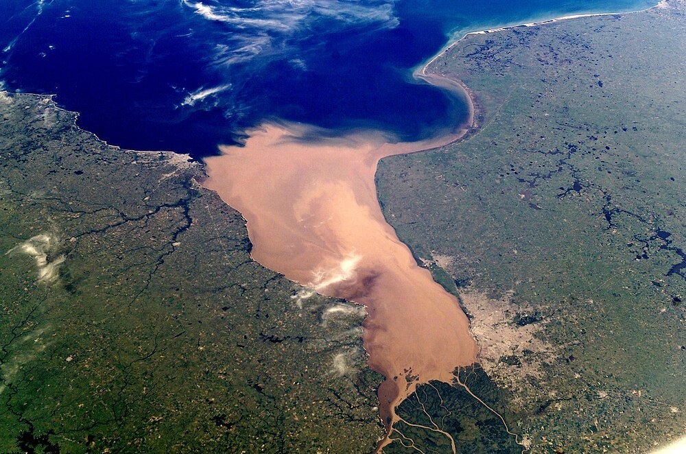 Aerial view of river delta meeting the sea Aerial view of a large river delta with muddy water flowing into a deep blue sea, surrounded by green and brown land areas.