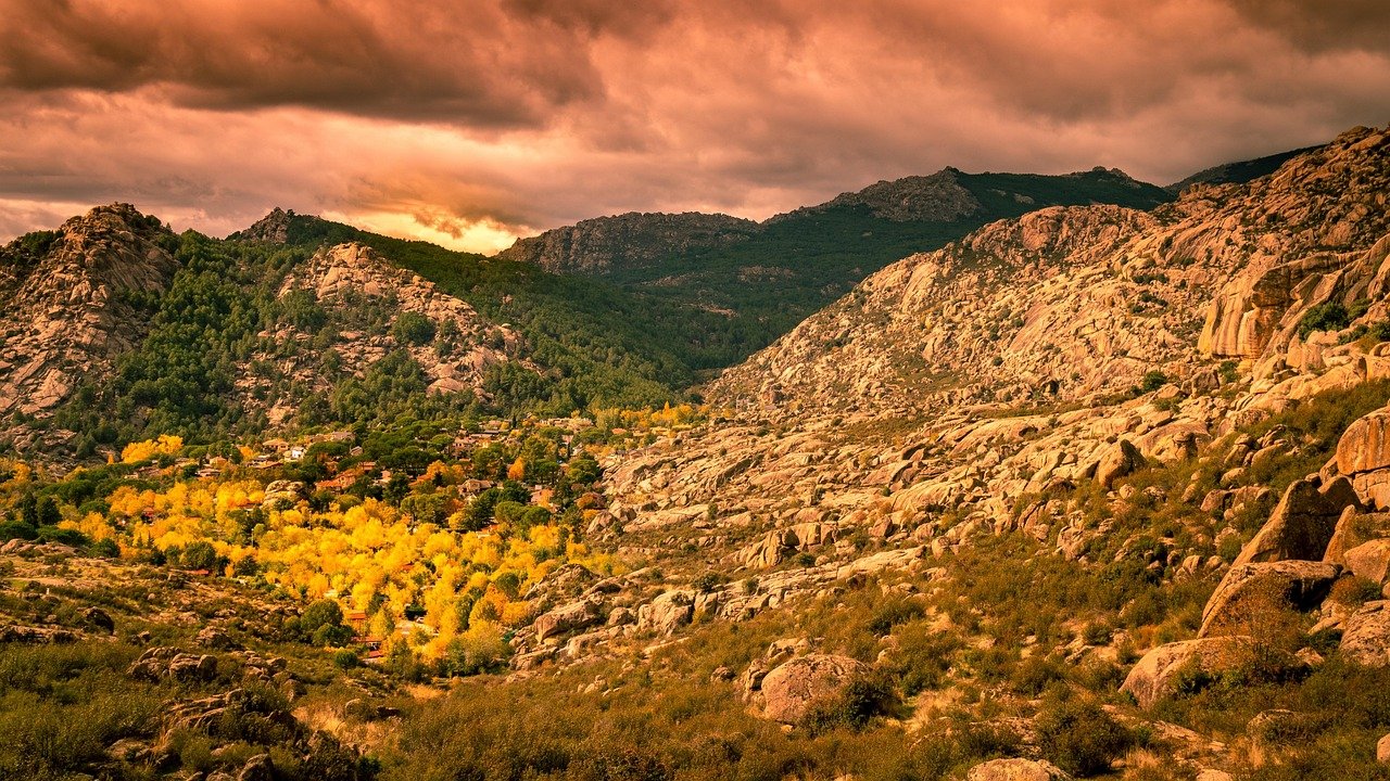 Rocky mountain landscape with dense green and yellow autumn trees under dramatic cloudy sky