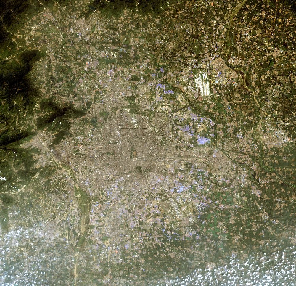 Satellite image of urban city and surrounding landscape Satellite view of a large urban city surrounded by agricultural fields and mountainous terrain with scattered clouds