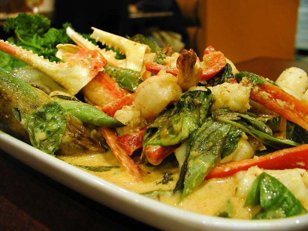 Seafood curry with crab claws and vegetables Delicious seafood curry with crab claws, shrimp, fresh spinach, and red bell peppers in creamy sauce on a white plate