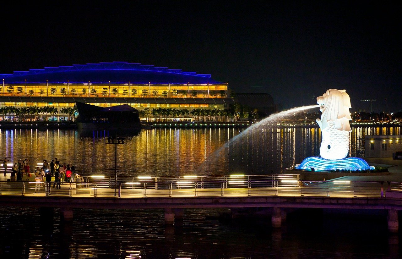 Night view of Singapore Merlion statue with water fountain and illuminated waterfront buildings reflecting on the water
