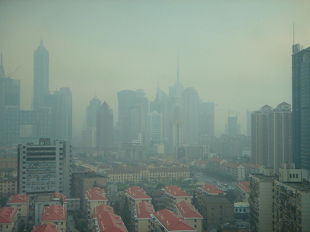 City skyline with tall buildings and red-roofed houses under heavy smog or fog, showing urban pollution and dense architecture