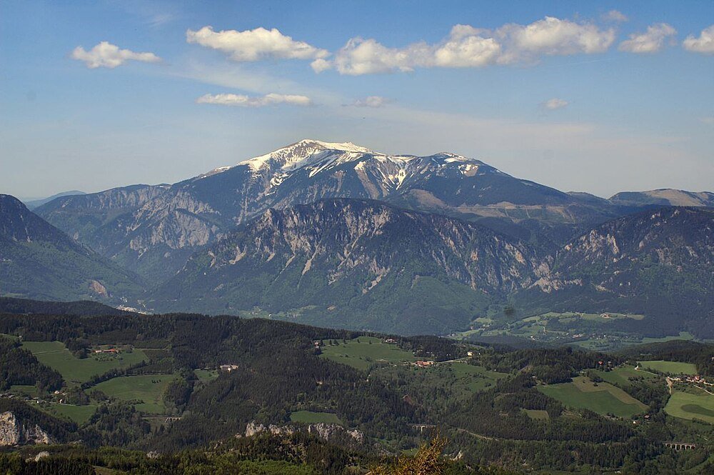 Snow-capped mountain and green valley landscape Scenic mountain landscape with snow-capped peaks, green valleys, and scattered clouds under a blue sky