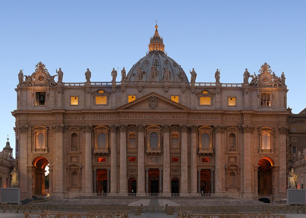 Front view of St. Peter's Basilica in Vatican City during sunset with illuminated windows and statues on the roof