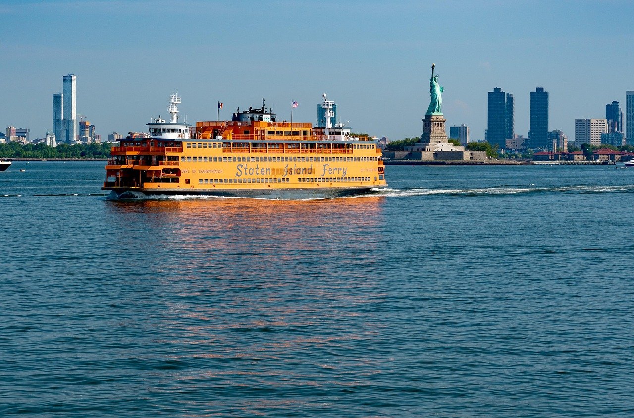 Staten Island Ferry cruising in New York Harbor with Statue of Liberty and city skyline in the background on a clear day