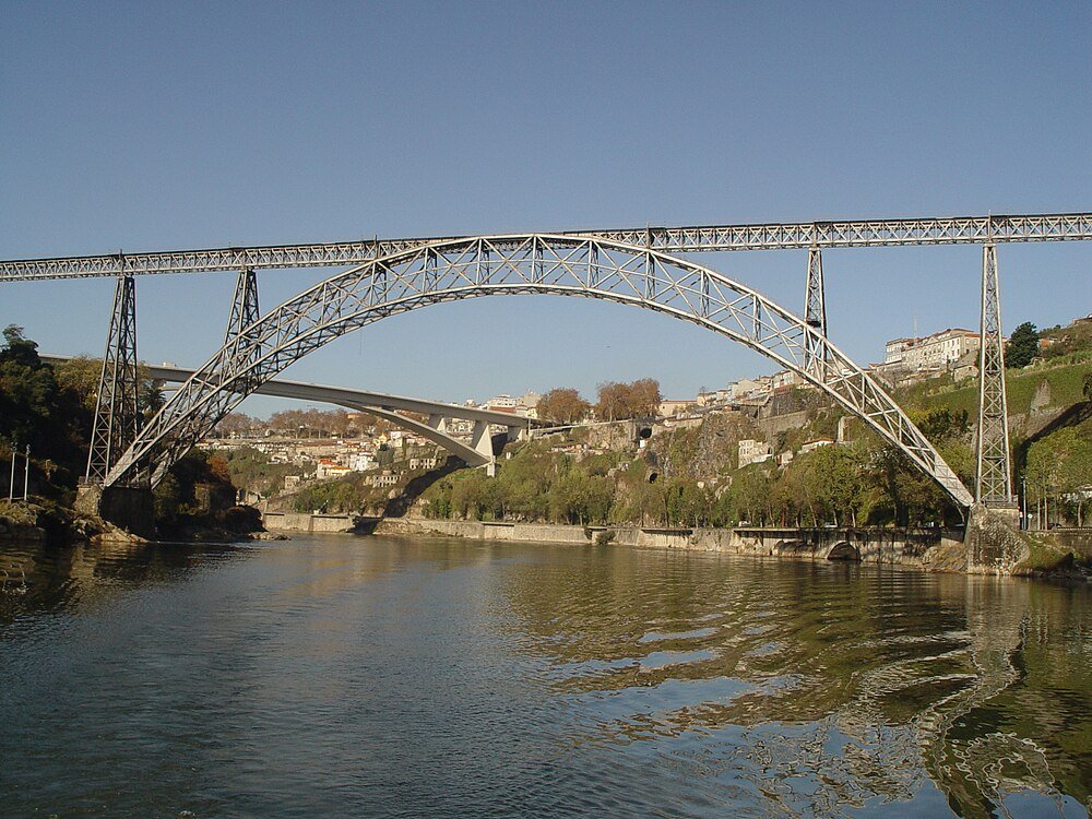 Steel Arch Bridge Over River with Urban Background Steel arch bridge over river with clear sky and urban landscape in the background, showcasing architectural design
