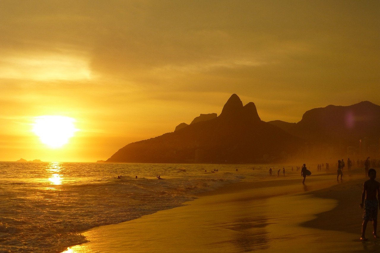 Sunset view of a crowded beach with waves, mountains, and people enjoying the golden hour by the sea
