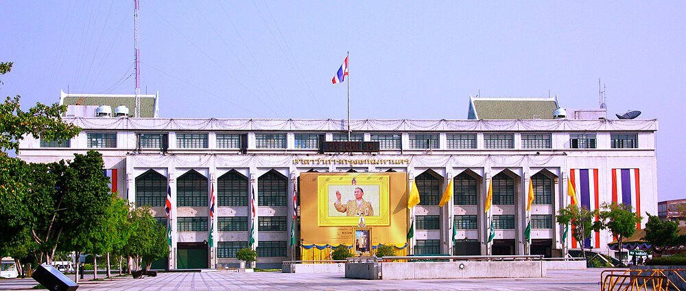 Thai government building with king's portrait and flags Government building in Thailand with large portrait of Thai king and national flags displayed prominently