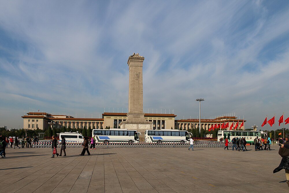 Tiananmen Square with Monument and Visitors Tiananmen Square in Beijing with Monument to the People's Heroes, buses, red flags, and tourists under a blue sky