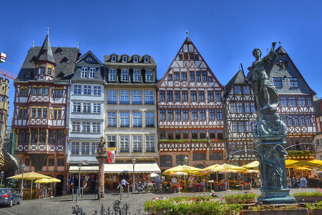 Historic timber-framed buildings and outdoor cafes with yellow umbrellas in a European town square on a sunny day