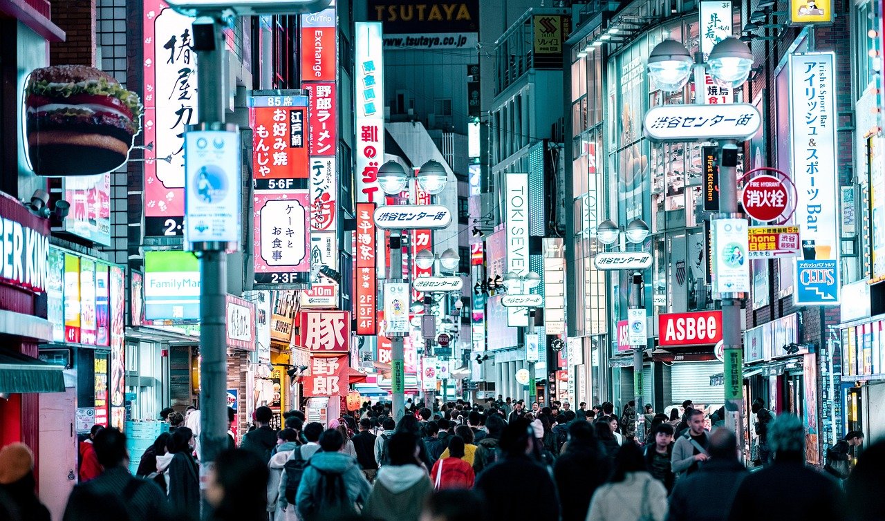 Crowded urban street in Tokyo at night with bright neon signs and diverse people walking under illuminated advertisements