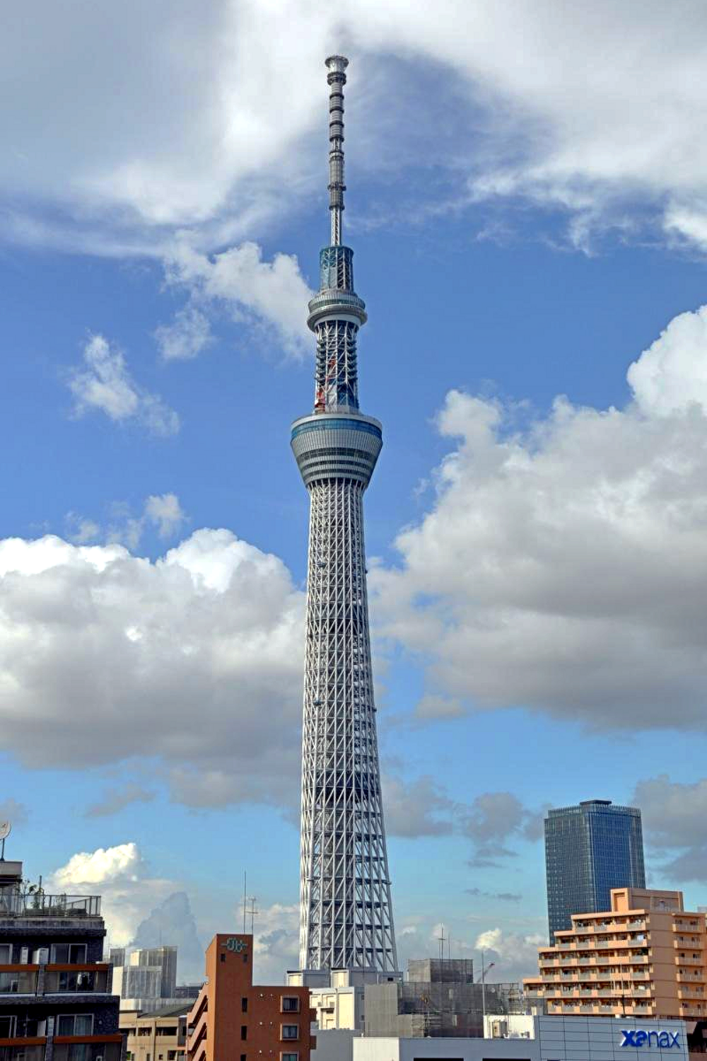Tokyo Skytree towering over city buildings under a blue sky with scattered clouds in Tokyo, Japan