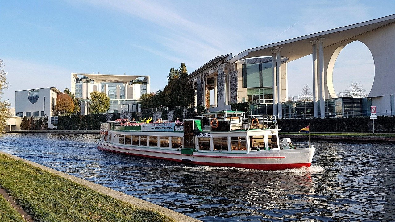 Tourist boat cruising on river with modern government buildings and clear sky in the background