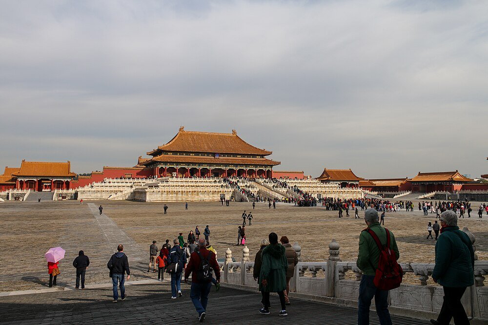 Tourists walking towards the Forbidden City in Beijing, China, with traditional Chinese architecture and cloudy sky
