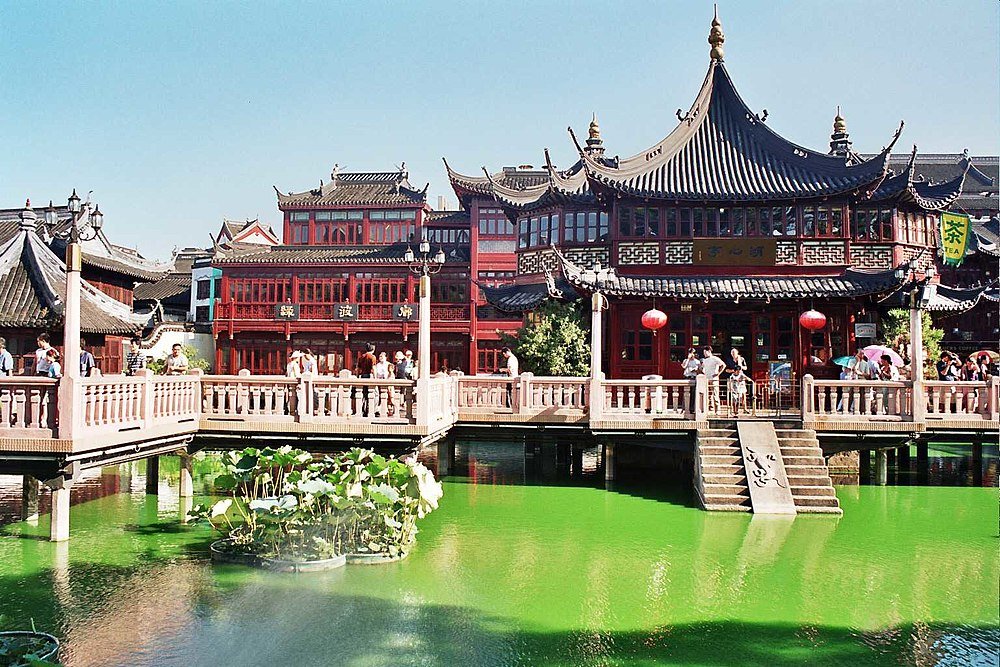 Traditional Chinese buildings and stone bridge over pond Traditional Chinese architecture with red wooden buildings and a stone bridge over a green pond with lotus plants