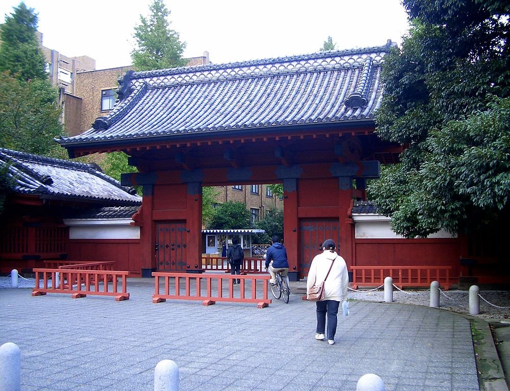 Traditional Japanese red gate with tiled roof Traditional Japanese red gate with tiled roof and people walking and cycling nearby in urban setting