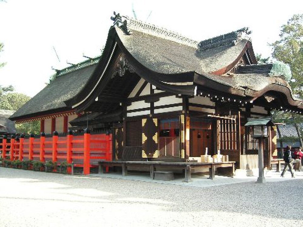 Traditional Japanese Shrine with Thatched Roof Traditional Japanese shrine with curved thatched roof and vibrant red wooden fence in a serene outdoor setting