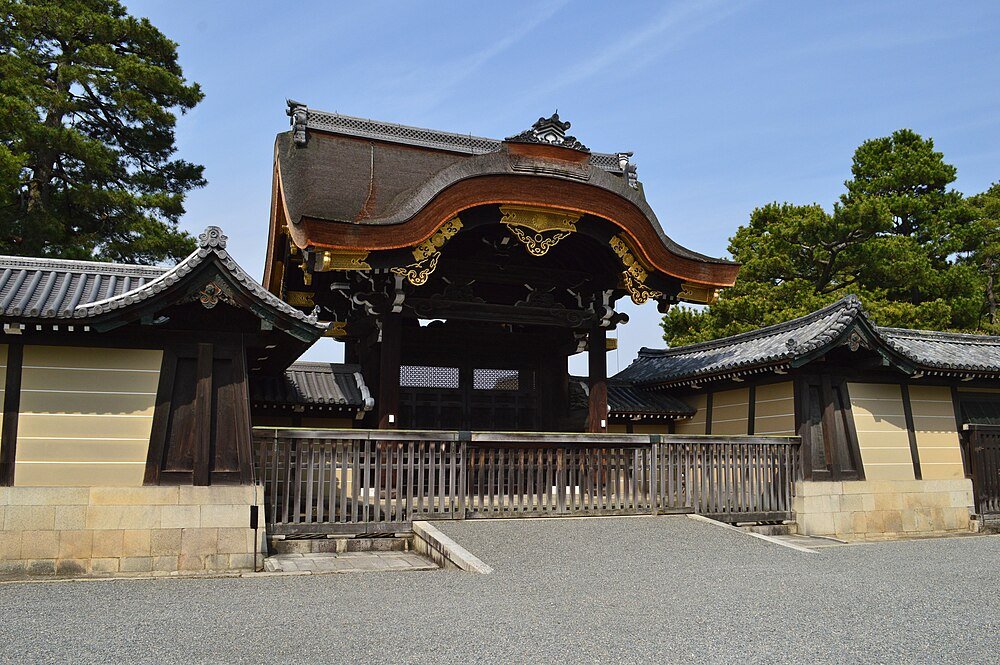 Traditional Japanese temple gate with ornate wooden roof and surrounding walls under clear blue sky