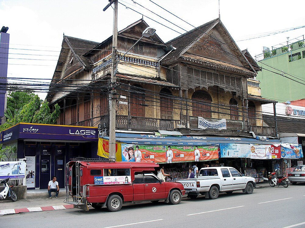 Traditional wooden building with shops and vehicles Old wooden building with traditional architecture above modern shops and vehicles on a busy street in Southeast Asia