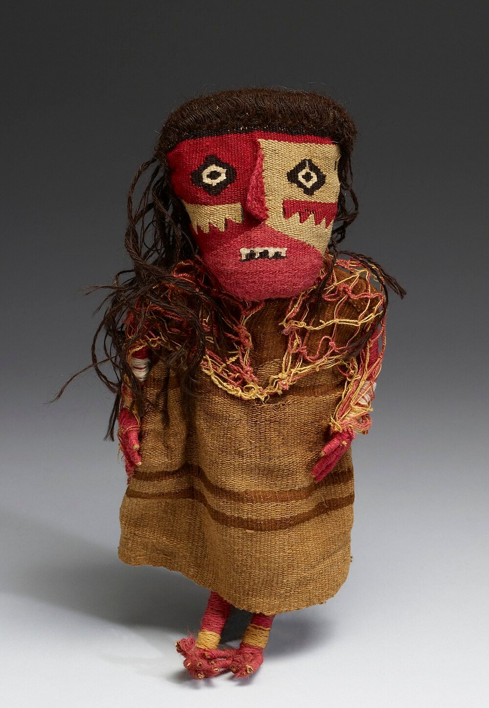 Handcrafted tribal textile doll with woven clothing Handcrafted tribal textile doll with red and beige face, brown hair, and woven brown clothing, showcasing traditional indigenous art.